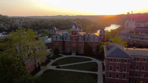 Aerial view of a historic brick building at sunset, surrounded by greenery and a river in the background.