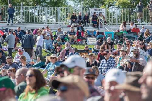 A large crowd of people sitting on bleachers at an outdoor event, enjoying the sunny day.