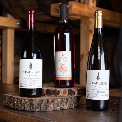 Three bottles of Cedar Ridge wine on a wooden surface, featuring red and white varieties with distinct labels.