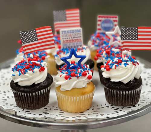 A platter of festive cupcakes topped with red, white, and blue decorations and small American flags.