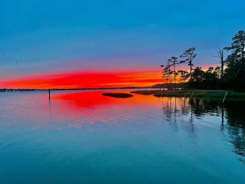 A vibrant sunset over a calm lake, reflecting shades of orange, pink, and blue, with silhouettes of trees along the shore.
