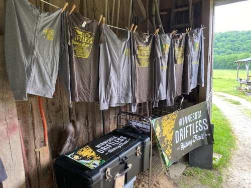 Gray shirts hanging on a line in a barn, promoting the Minnesota Driftless Hiking Trail. A banner is nearby.