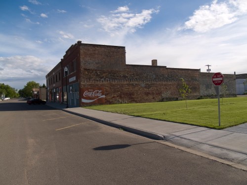 A quiet street scene featuring a brick building with a vintage Coca-Cola advertisement and a "Do Not Enter" sign.