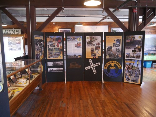 Exhibit display featuring historical photos and information about a railroad crossing, set in a wooden interior.