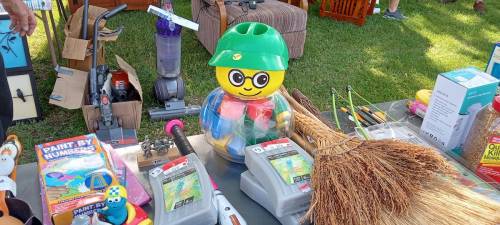 A colorful toy figure wearing a green helmet stands among various items on a table, including paint kits and cleaning tools.