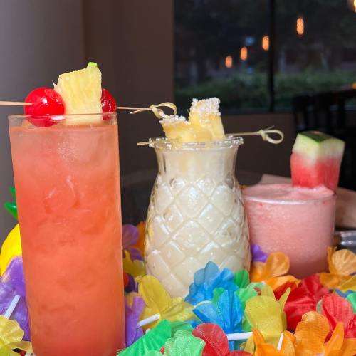 A colorful display of tropical cocktails with garnishes, surrounded by vibrant flower-shaped decorations.