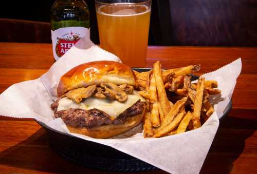 A juicy burger with melted cheese and mushrooms, served with crispy fries and a glass of beer on a wooden table.