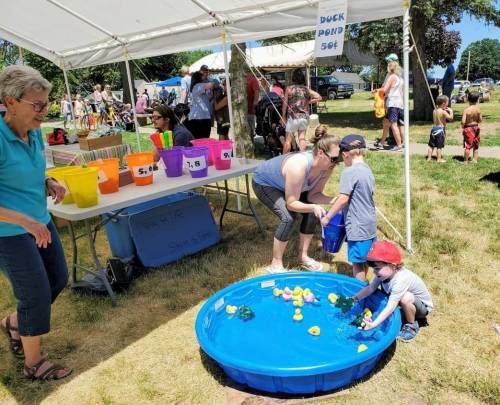A summer fair scene with kids playing in a duck pond game, adults supervising, and colorful buckets nearby.