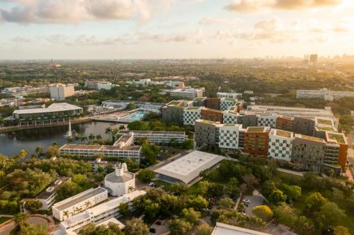 Aerial view of a modern campus surrounded by greenery and a lake, with city skyline in the background at sunset.