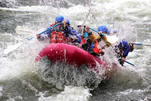 A group of people in a pink raft navigating turbulent waters, splashing water around them as they paddle.