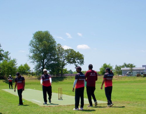 A group of players in red and black jerseys walking on a cricket field under a clear blue sky.