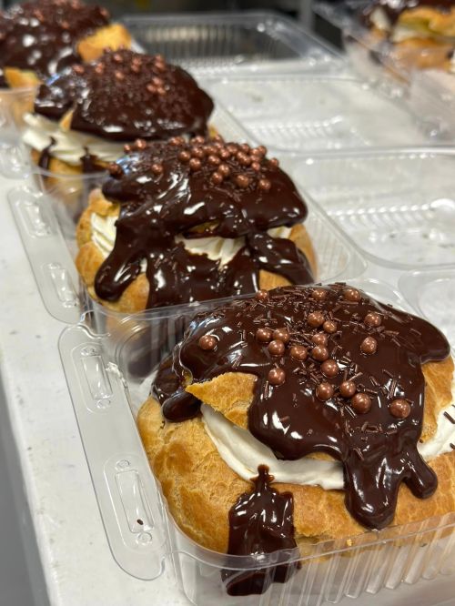 Delicious cream-filled pastries topped with chocolate sauce and decorative chocolate balls in clear containers.