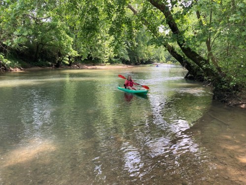 A person kayaking on a calm river surrounded by lush green trees and clear water.