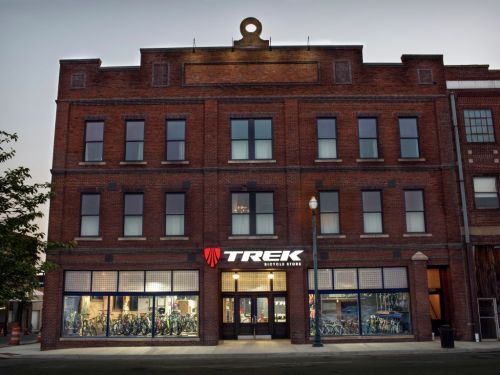 Exterior of a brick building featuring a Trek bicycle store, with large windows displaying bicycles inside.