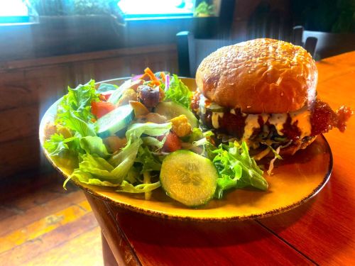 A plate with a crispy chicken sandwich topped with sauce, alongside a fresh salad with mixed greens and vegetables.