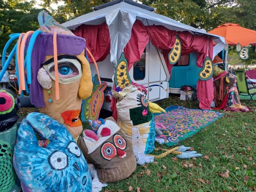 Colorful, whimsical decorations and art pieces adorn a camper, surrounded by vibrant patterns and greenery.