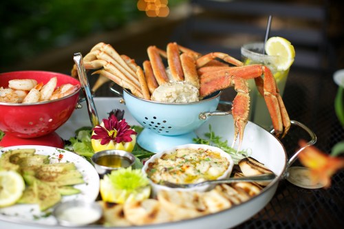 A seafood platter featuring crab, shrimp, avocado, and a creamy dip, garnished with lemon and flowers.