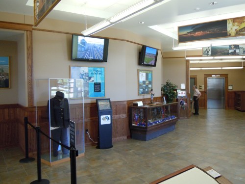 Interior of a visitor center featuring displays, an elevator, and a person standing near a glass exhibit.