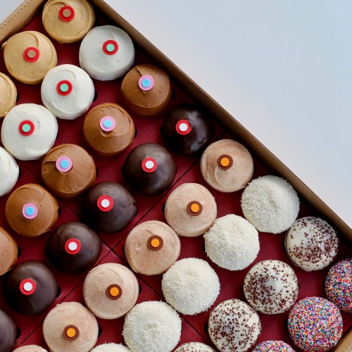 A colorful assortment of cupcakes in a box, featuring various frosting styles and toppings.