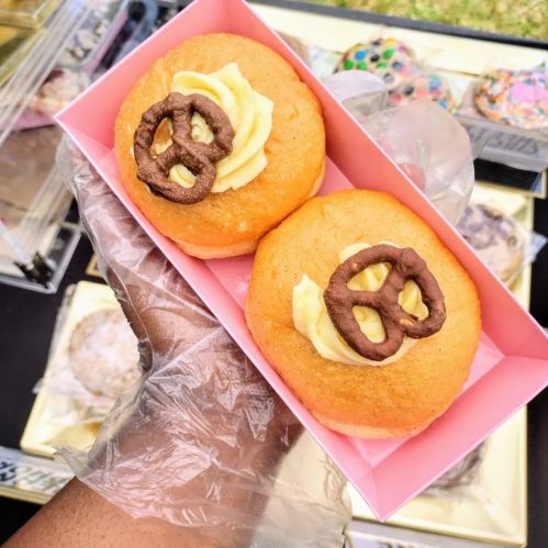 A hand holding a pink box with two sweet buns topped with frosting and pretzel pieces.