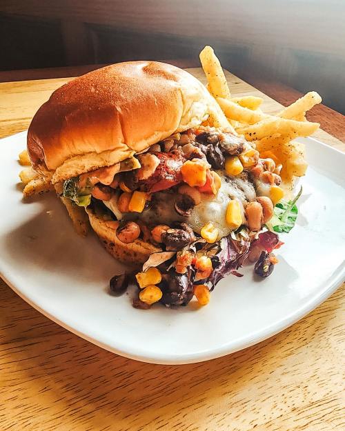 A hearty burger topped with beans, corn, and lettuce, served with a side of crispy fries on a white plate.