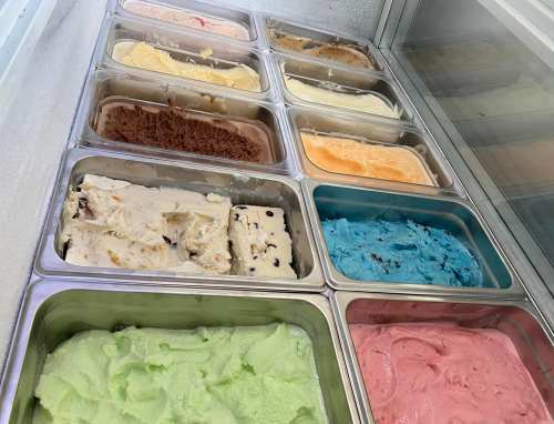 A display of various ice cream flavors in metal containers, including chocolate, mint, and strawberry.