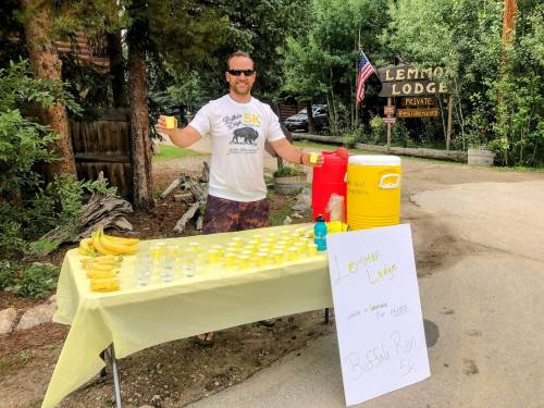 A man stands behind a table with cups and bananas, promoting a lemonade stand for a local 5K event near Lemon Lodge.