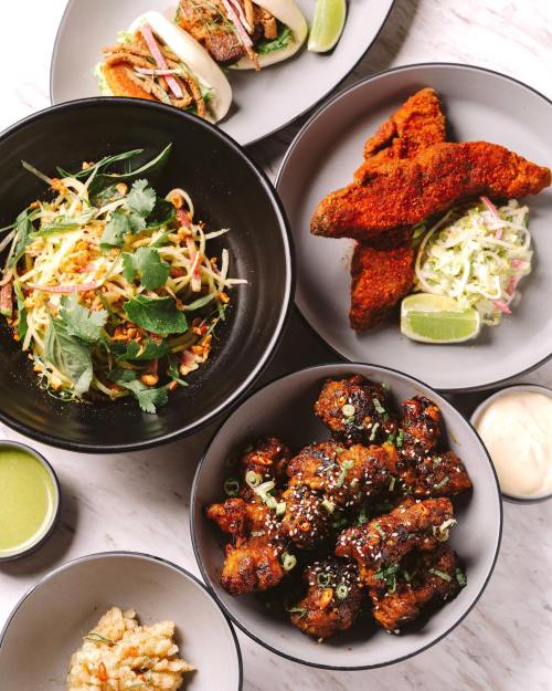 A vibrant spread of Asian-inspired dishes, including tacos, fried chicken, salad, and dipping sauces on a marble table.