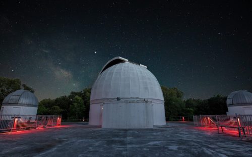 A dome-shaped observatory under a starry night sky, with red lights illuminating the surrounding area.