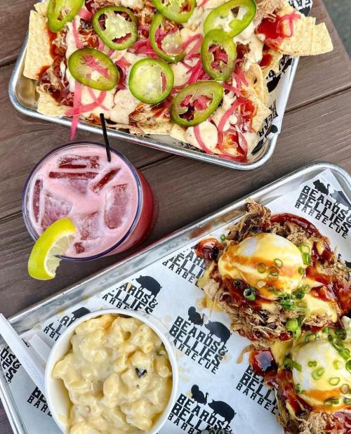 A tray of nachos topped with jalapeños and pickled onions, alongside a drink and a plate of pulled pork eggs benedict.