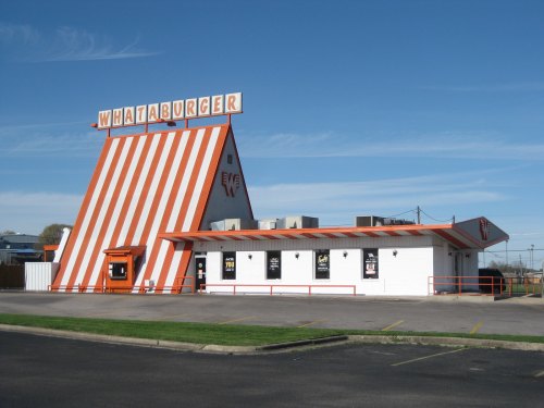 A Whataburger restaurant with a distinctive orange and white striped A-frame design against a clear blue sky.