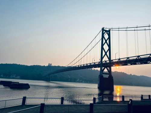 A bridge spans a river at sunset, with hills in the background and calm water reflecting the light.