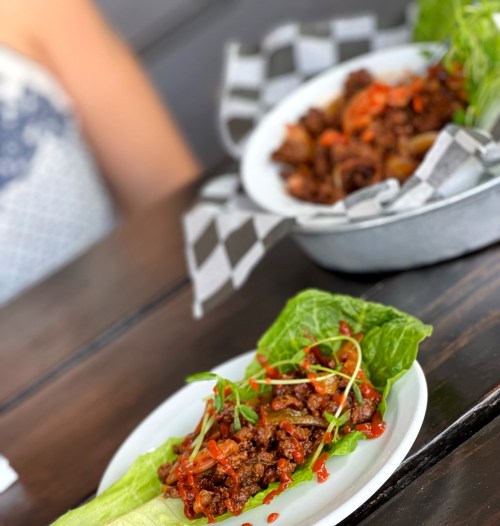 Two plates of food: one with lettuce wraps filled with meat and vegetables, and another bowl of meat with sauce.