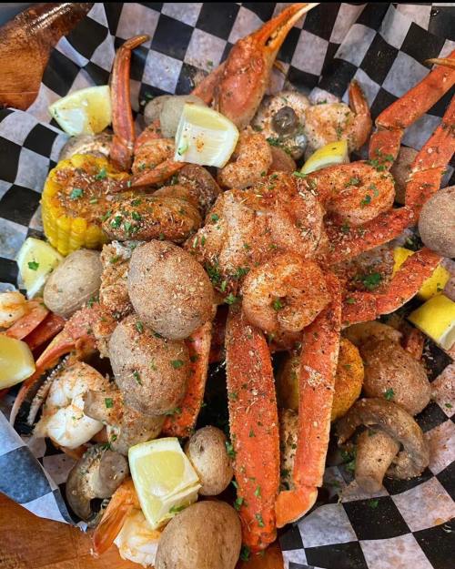 A seafood platter featuring crabs, shrimp, corn, potatoes, and lemon wedges, garnished with herbs and spices.