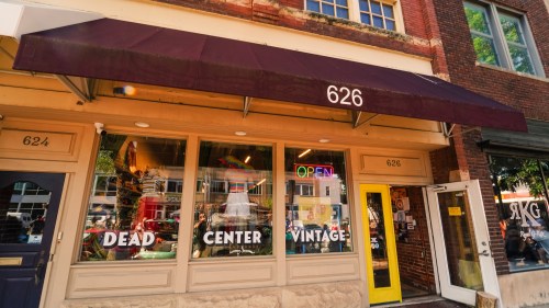 A vintage shop with a maroon awning, large windows displaying clothes, and an "OPEN" sign. Address: 626.