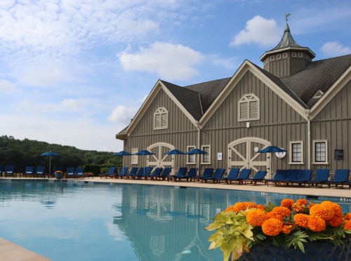 A serene poolside view with blue lounge chairs, a flower pot, and a charming building under a partly cloudy sky.