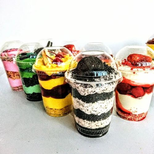 Colorful layered desserts in clear cups, featuring various flavors and toppings, arranged in a row against a white background.