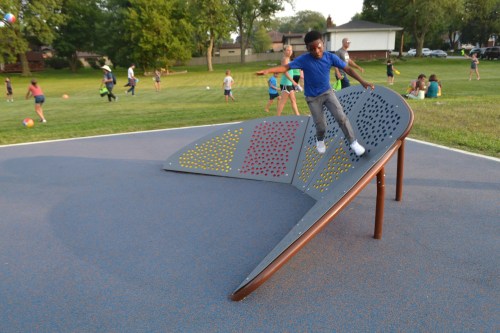 A child plays on a colorful climbing structure in a park, with other kids and activities in the background.