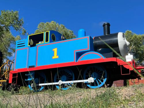 A colorful model train resembling a cartoon character, with a blue body and red accents, set against a clear blue sky.