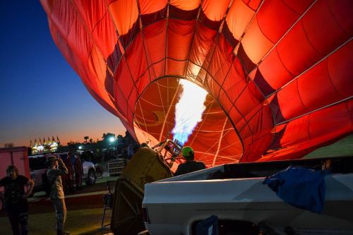 A hot air balloon being inflated at dusk, with flames igniting inside and a truck nearby.