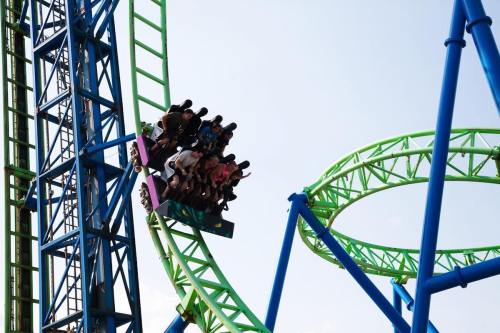 A group of people enjoying a thrilling ride on a roller coaster with green and blue tracks against a clear sky.