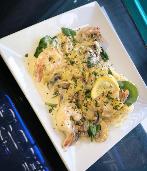 A plate of creamy shrimp pasta with mushrooms, spinach, and lemon slices, garnished with parsley.
