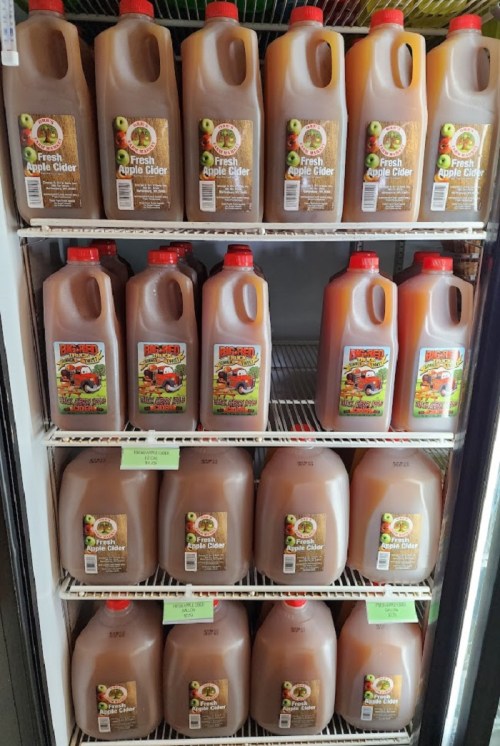 Shelves filled with jugs of fresh apple cider, labeled and organized in a refrigerated display.