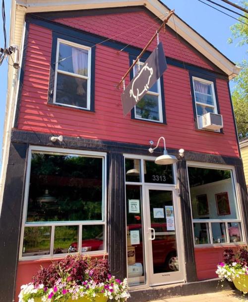 A red and black building with large windows, a sign hanging above the entrance, and colorful flowers in front.