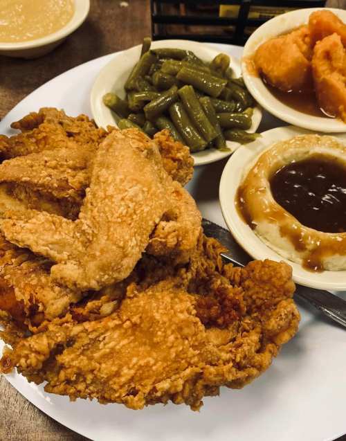 A plate of crispy fried chicken with green beans, mashed potatoes with gravy, and sweet potato on the side.