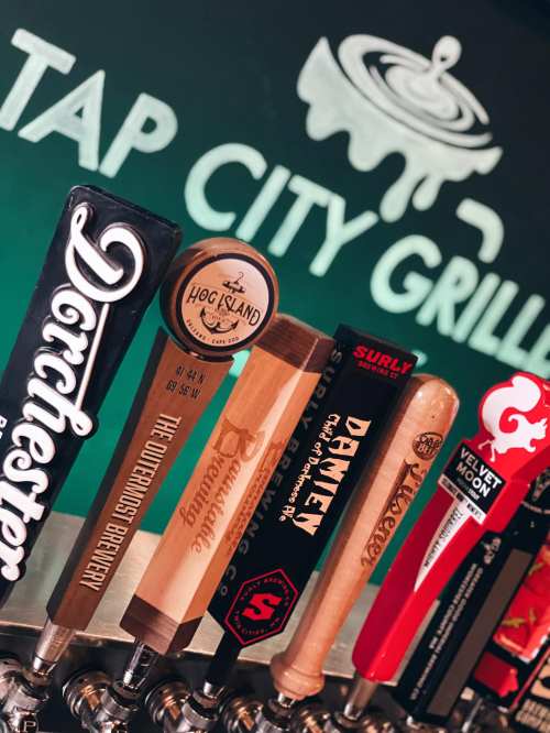 A row of beer taps with various brewery logos at Tap City Grille, featuring a variety of craft beers.