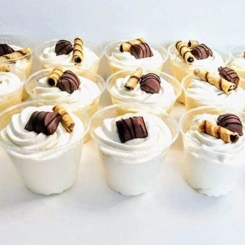 A row of dessert cups filled with whipped cream, topped with chocolate and rolled wafer sticks.