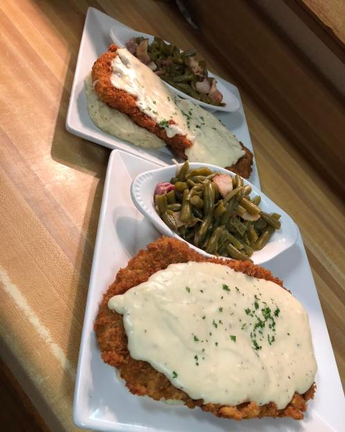 Three plates of crispy fried chicken topped with creamy white gravy, served with a side of green beans.