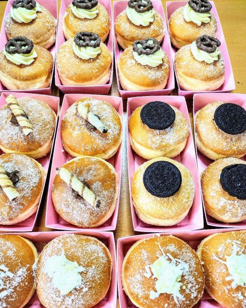 A variety of donuts in pink boxes, topped with cream, chocolate, and cookies, arranged neatly on a table.