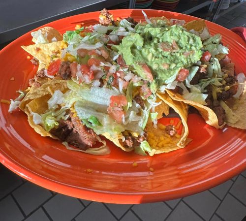 A vibrant orange plate filled with loaded tacos topped with guacamole, lettuce, and diced tomatoes.